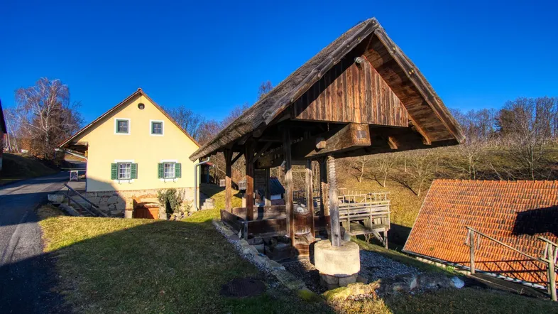 Ländliches Anwesen mit traditionellem Holzbrunnen und gelbem Gebäude unter blauem Himmel.