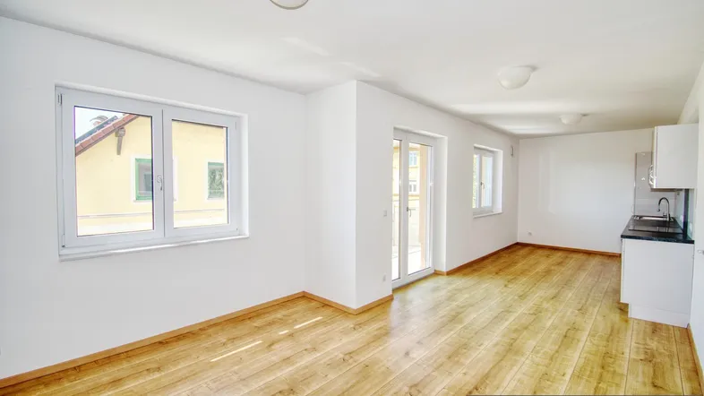 Heller, offener Wohnbereich mit Holzfußboden und Zugang zum Balkon, inklusive Küchenzeile.