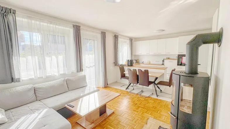 Helles, offenes Wohn-Esszimmer mit integrierter Küche, Kaminofen und Zugang zum Balkon.