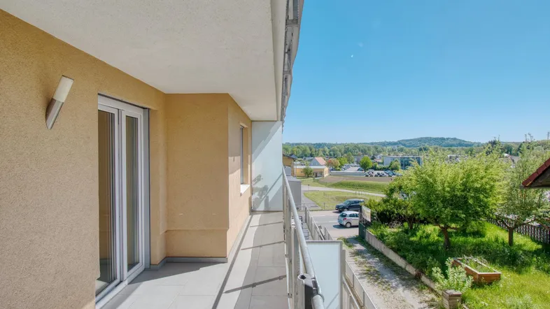 Heller Balkon mit Fliesenboden und Geländer, bietet einen weiten Blick ins Grüne.