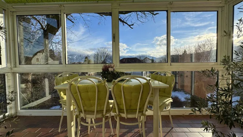 Heller Wintergarten mit Terracotta-Fliesenboden, Gartenmöbeln und weitem Bergblick.