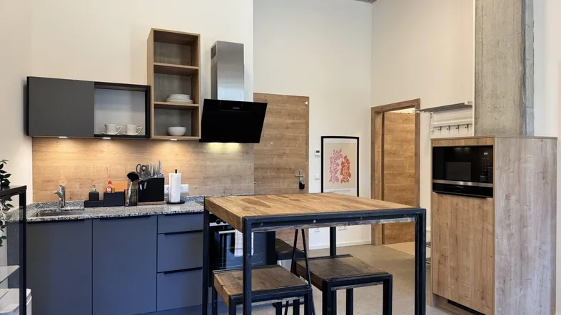 Moderne Küche mit grauen Schränken, Holzrückwand und einer Bartheke mit Hockern.