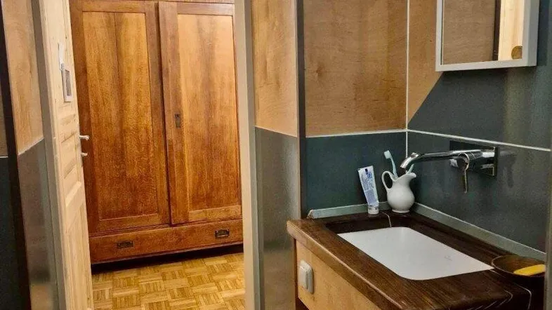 Kleines Badezimmer mit Holzwaschtisch, Spiegel und Zugang zu einem weiteren Raum.
