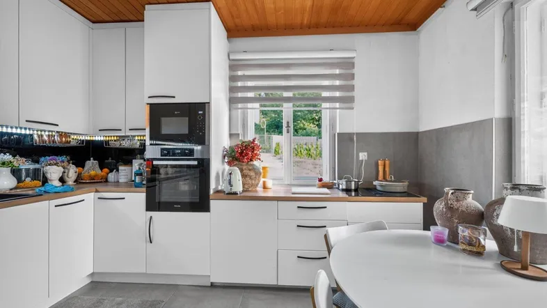 Moderne Küche mit weißen Schränken, Holzbalkendecke und integrierten Geräten, ideal für gemeinsame Mahlzeiten.