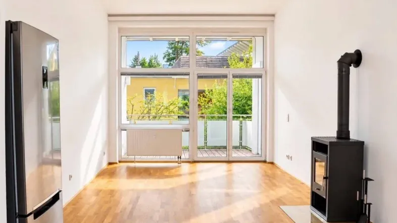 Helles Wohnzimmer mit Holzboden, Kaminofen und großem Fenster mit Zugang zum Balkon.