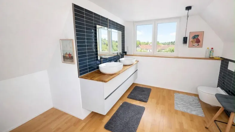 Modernes Badezimmer im Dachgeschoss mit Doppelwaschbecken, Holzplatte und Fenster mit Ausblick.