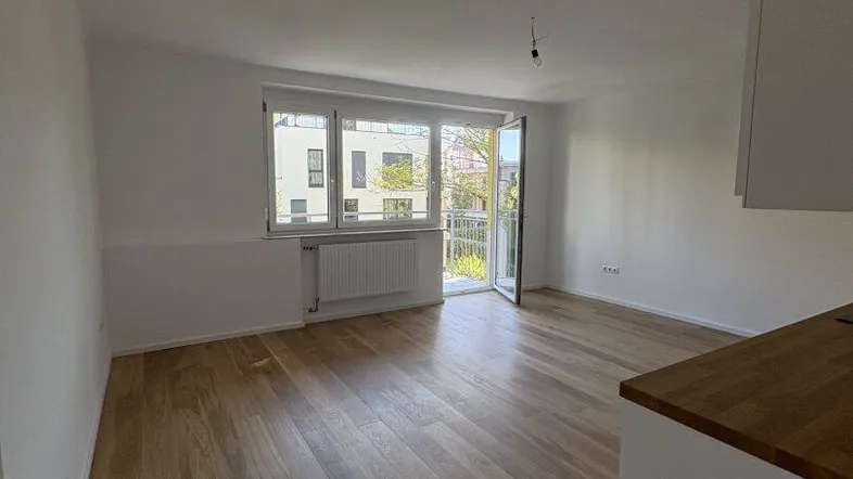 Helles Wohnzimmer mit Holzboden, großen Fenstern und Zugang zu einem Balkon.