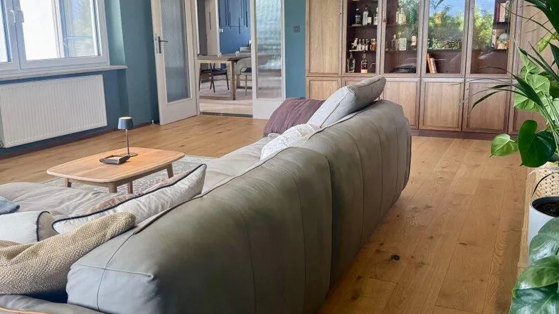 Geräumiges Wohnzimmer mit bequemer Couch, Holzboden und einer Decke mit interessanter Kassettenoptik.