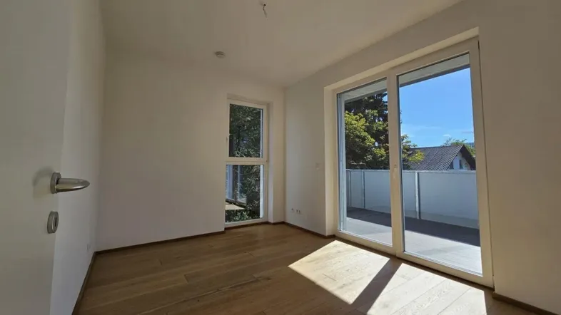 Helles Zimmer mit Holzboden und Zugang zu einer Terrasse, bietet viel natürliches Licht.