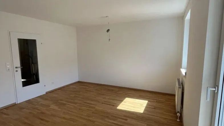 Heller, leerer Raum mit Holzboden und großen Fenstern, ideal als Wohnzimmer.