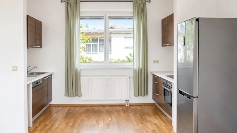 Helle Küche mit Holzschränken, einem modernen Kühlschrank und Blick ins Grüne.