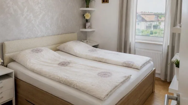 Helles Schlafzimmer mit Holzbett, Parkettboden und Fenster mit Blick ins Grüne.