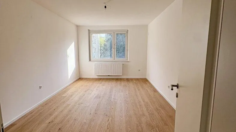 Helles, leeres Zimmer mit neuem Holzboden und Fensterblick, bereit zum Einzug.