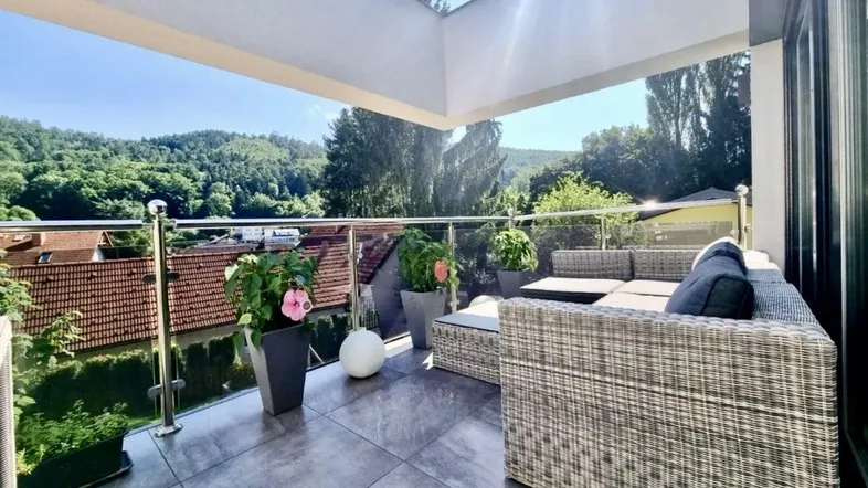 Geräumige Terrasse mit modernen Loungemöbeln, Glasgeländer und weitem Blick ins Grüne.
