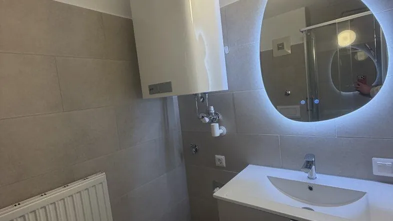Modernes Badezimmer mit Waschbecken, beleuchtetem Spiegel und Wandheizkörper.