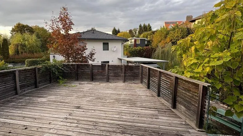 Große Holzterrasse mit Blick auf das umliegende Wohngebiet und herbstliche Bäume unter bewölktem Himmel.