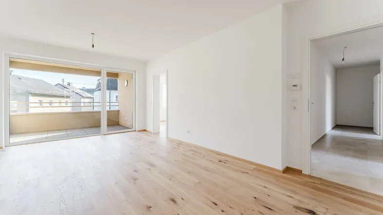 Helles Wohnzimmer mit neuem Holzboden und Zugang zu einem Balkon, bietet viel natürliches Licht.