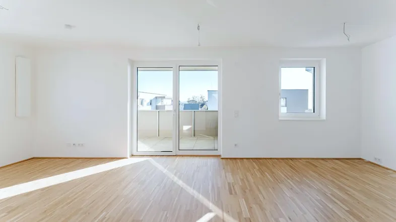 Helles, leeres Zimmer mit Parkettboden und Zugang zu einem Balkon, ideal für Wohn- oder Schlafbereich.
