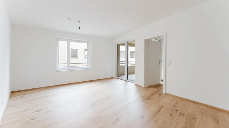 Helles, leeres Zimmer mit neuem Holzboden und Zugang zu einem Balkon, ideal für Wohn- oder Schlafbereich.