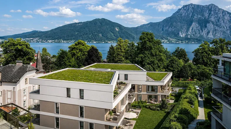 Moderne Wohngebäude mit begrünten Dächern und Seeblick vor einer beeindruckenden Bergkulisse.