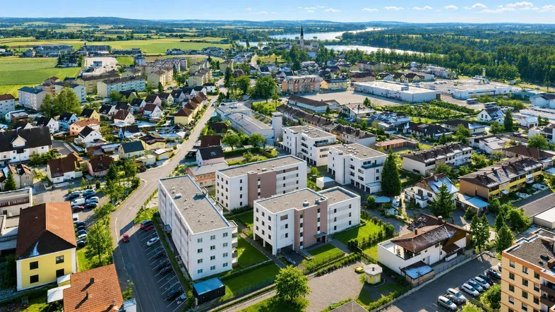 Luftaufnahme einer Wohnsiedlung mit modernen Gebäuden, umgeben von grünen Feldern und einem See.
