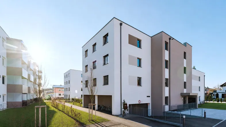 Moderne Wohngebäude mit heller Fassade, Tiefgaragenzufahrt und gepflegten Grünflächen unter blauem Himmel.