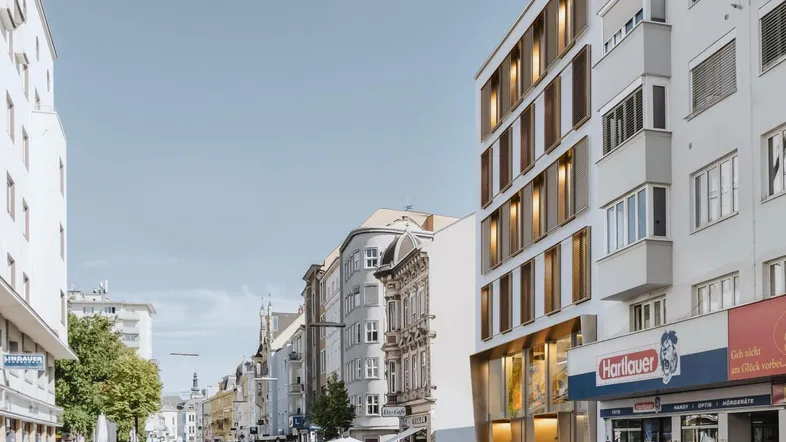 Moderne Gebäude entlang einer belebten Stadtstraße mit Geschäften und Straßenbahnschienen unter klarem Himmel.