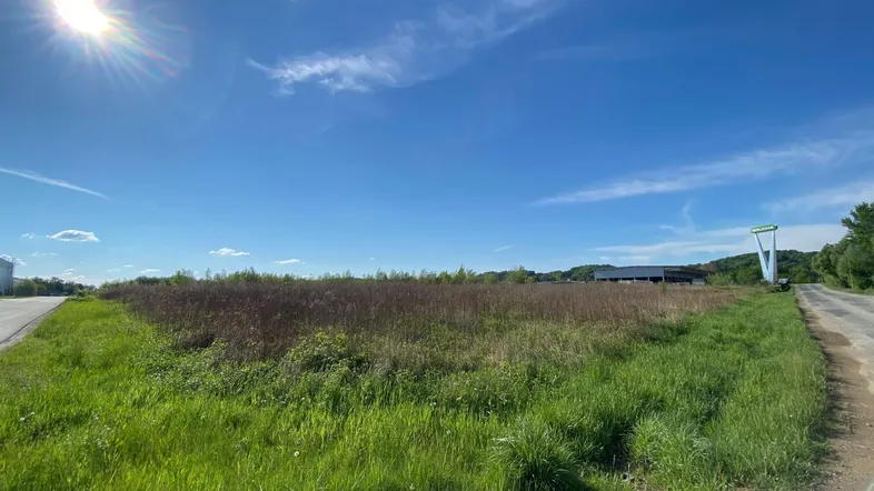 Weitläufiges unbebautes Grundstück mit Gras und trockener Vegetation unter blauem Himmel.