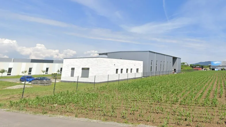 Modernes Gewerbegebäude mit heller Fassade und angrenzendem Feld unter blauem Himmel.