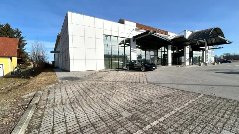 Modernes Geschäftsgebäude mit großer Glasfassade und weitläufigem Parkplatzbereich unter blauem Himmel.