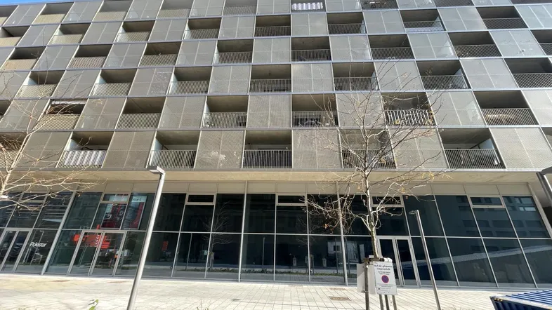 Moderne Gebäudefassade mit vielen Balkonen und großen Fensterfronten im Erdgeschoss, typisch für einen Neubau.