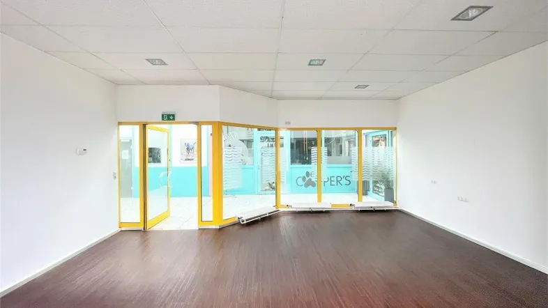 Geräumiger, leerer Gewerberaum mit dunklem Laminatboden und großen Glasfronten, ideal für ein Geschäft.