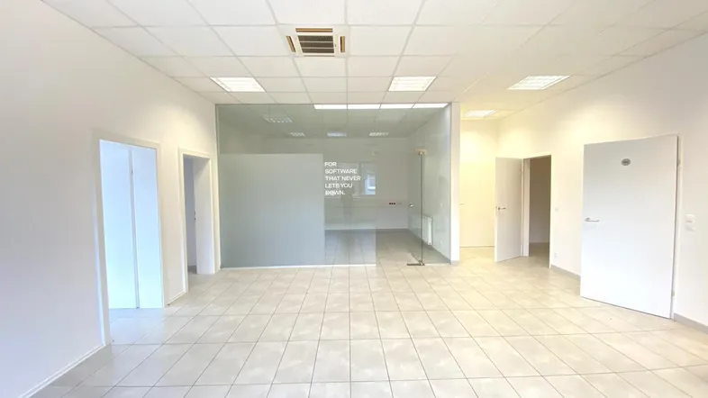 Geräumiger Büroraum mit Fliesenboden, abgehängter Decke und einer Glasabtrennung zu einem weiteren Bereich.