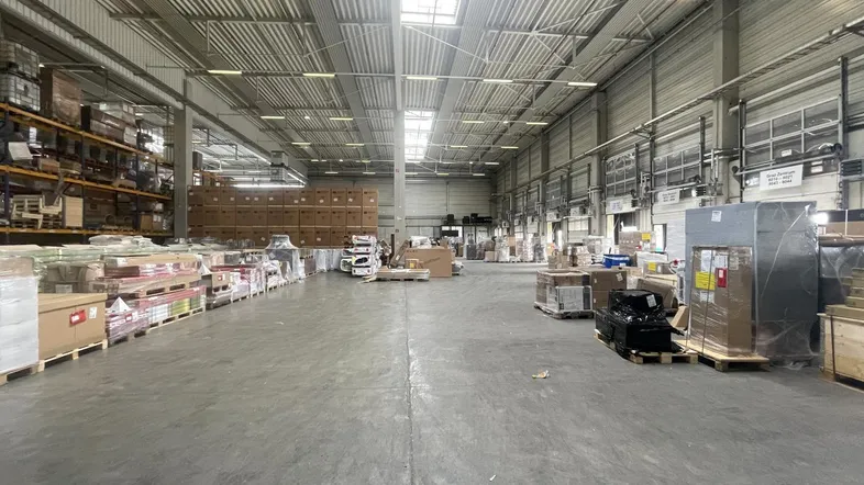 Geräumige Lagerhalle mit hohen Decken, Betonboden und natürlichem Lichteinfall durch Oberlichter.