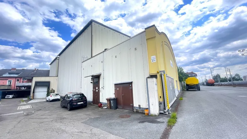 Großes Industriegebäude mit heller Fassade und Parkplätzen unter bewölktem Himmel.