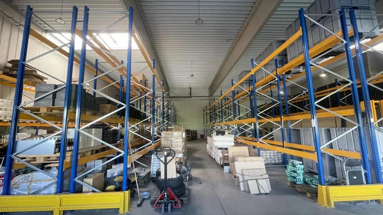 Geräumige Lagerhalle mit hohen Decken, robusten Metallregalen und ausreichend Platz für Warenlagerung und Logistik.