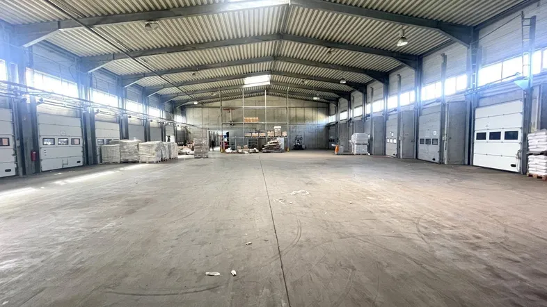 Geräumige Lagerhalle mit Betonboden, hohen Decken und mehreren Rolltoren für den Warenumschlag.