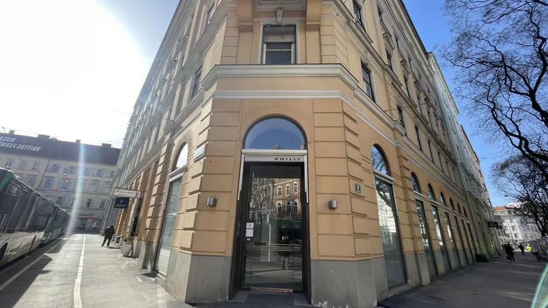 Historisches Eckgebäude mit großen Schaufenstern und Eingangsbereich in einer belebten Stadtlage.