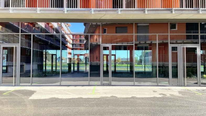 Moderne Gebäudefassade im Erdgeschoss mit großen Glasfronten, die die oberen orangefarbenen Etagen widerspiegeln.