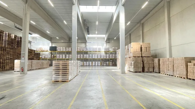 Geräumige Lagerhalle mit hohen Decken, Betonboden und viel Tageslicht durch Oberlichter.