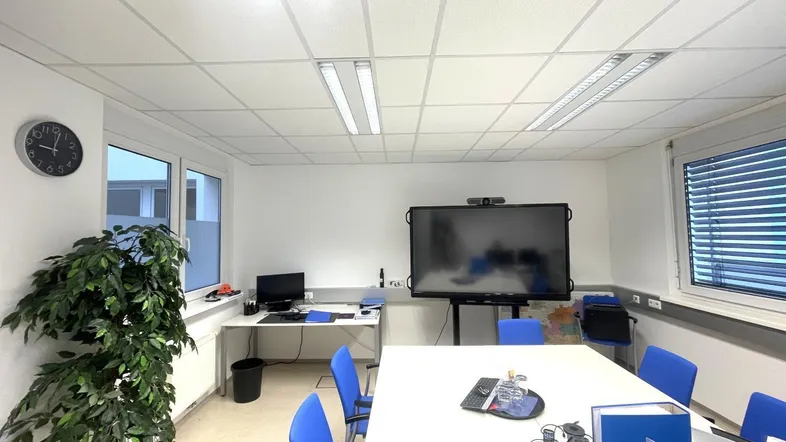 Moderner Konferenzraum mit großem Bildschirm, Besprechungstisch und viel Tageslicht durch große Fenster.