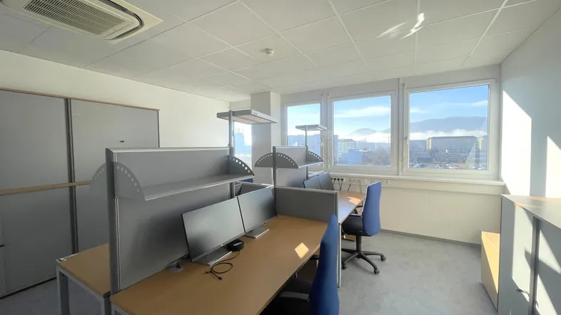 Heller Großraumbüro mit modernen Arbeitsplätzen, Klimaanlage und weitem Ausblick durch große Fenster.