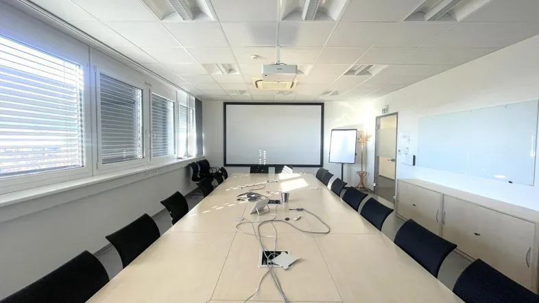 Geräumiger Konferenzraum mit großem Tisch, Projektor und Whiteboard, ideal für Besprechungen.