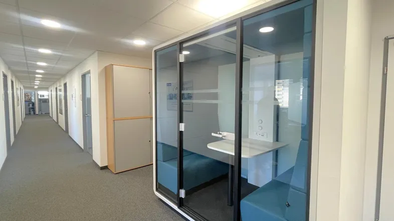 Langer Bürogang mit Teppichboden und einer modernen, schallgedämmten Glaskabine für Besprechungen.