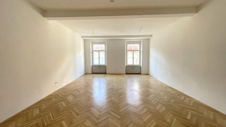 Geräumiger, leerer Raum mit Fischgrätparkettboden und zwei Fenstern, ideal für Wohnzwecke.