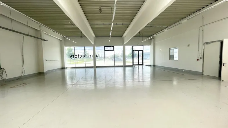 Geräumige, leere Gewerbefläche mit hohen Decken und großen Fenstern, die viel Tageslicht hereinlassen.