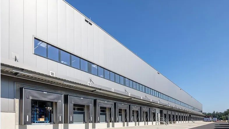 Moderne Industriehalle mit zahlreichen Laderampen und großen Fensterreihen unter klarem blauen Himmel.