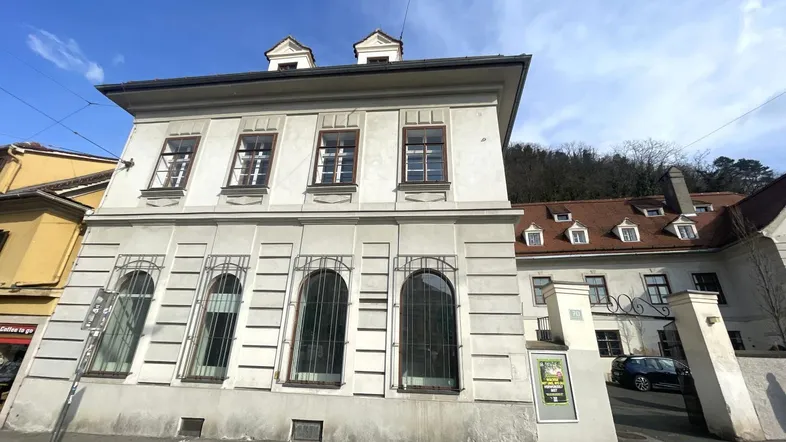 Historisches Gebäude mit klassischer Fassade und Bogenfenstern an einer städtischen Straße.