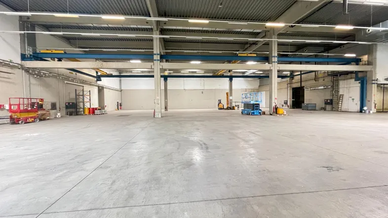 Geräumige Lagerhalle mit hoher Decke, Betonboden und sichtbaren Kranbahnen für industrielle Nutzung.