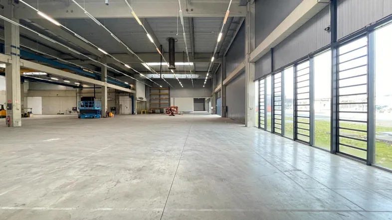 Geräumige Lagerhalle mit hohen Decken, großen Fenstern und Betonboden, ideal für industrielle Nutzung.